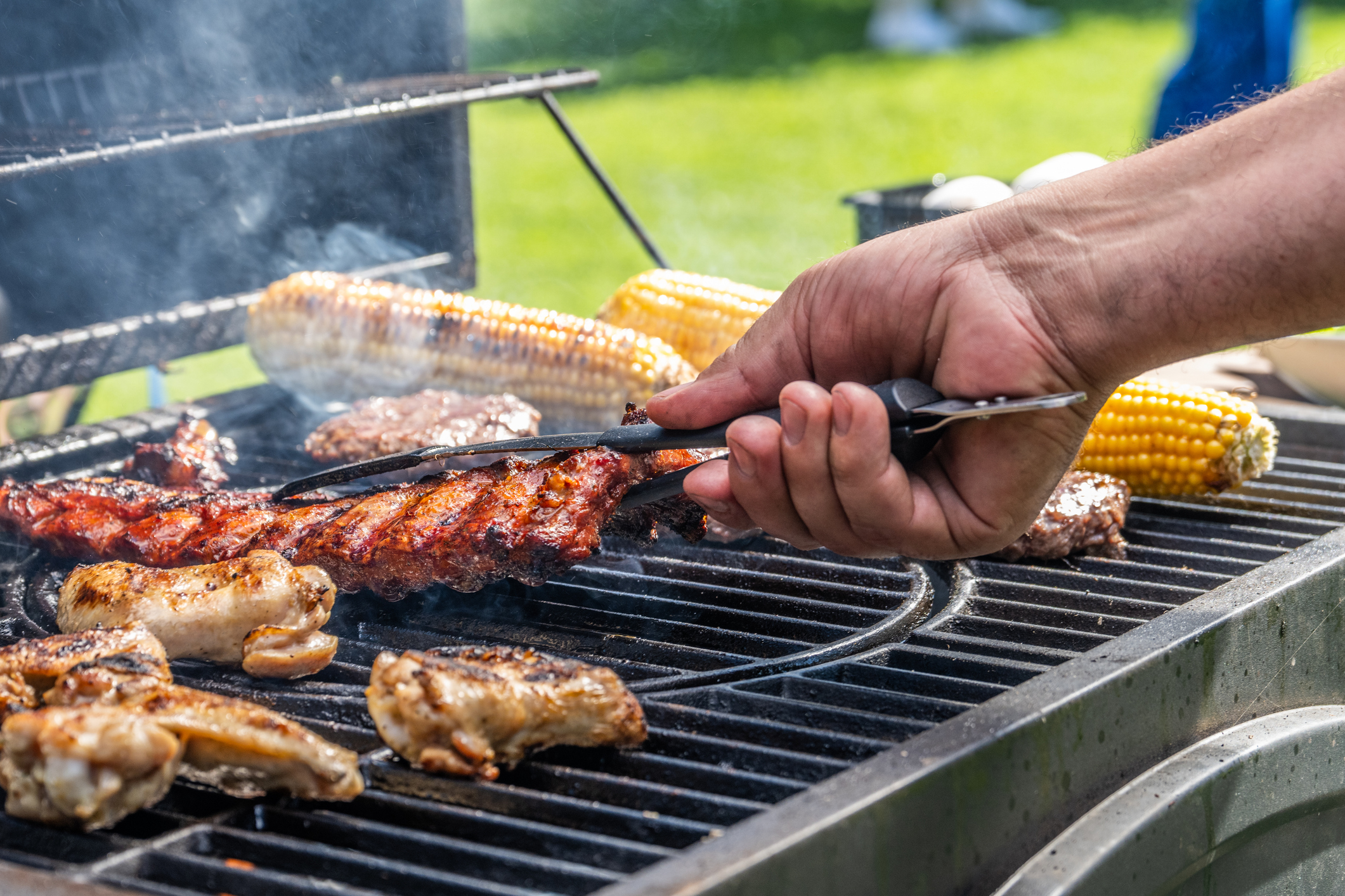 Man using tongs to take meat off grill