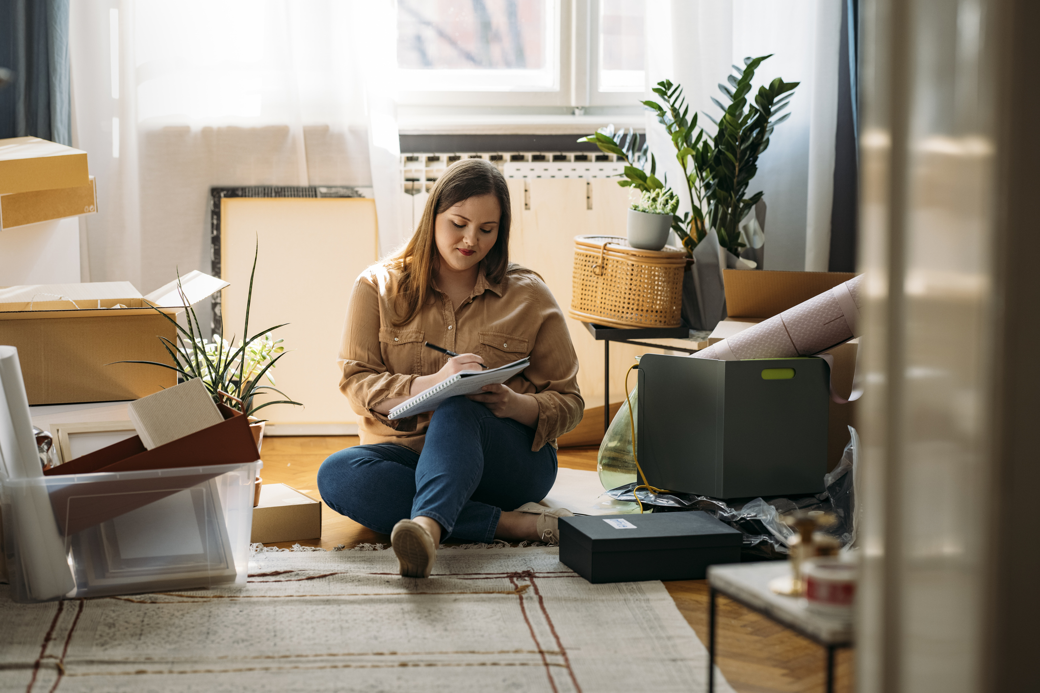 Moving Out: Beautiful Smiling Overweight Woman Sitting on the Floor Surrounded by Packed Boxes and Making a To-do List